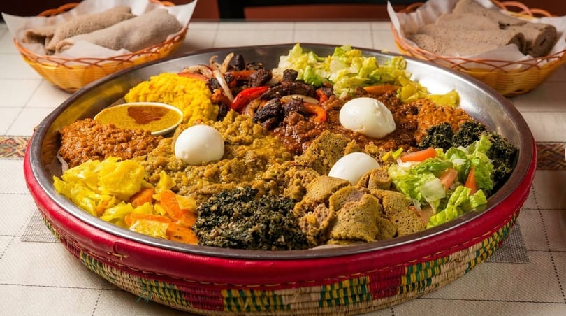 A large platter of colorful Ethiopian food, including injera, stews, vegetables, and hard-boiled eggs.