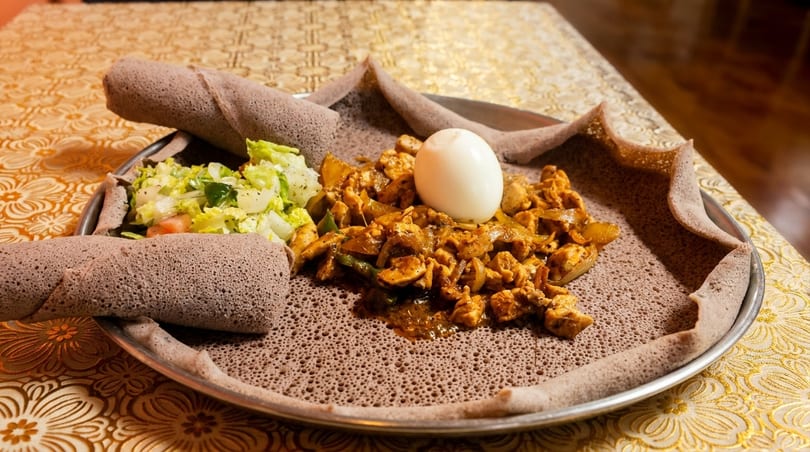 Ethiopian Doro Wat with injera, a hard-boiled egg, and a side salad on a metal platter.