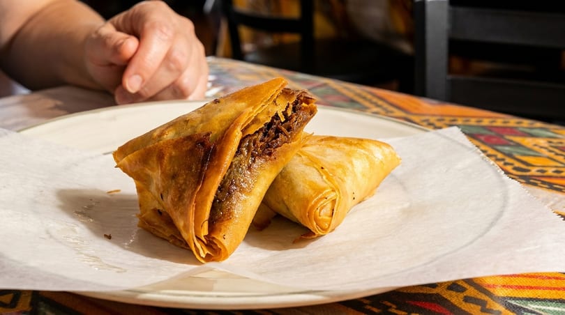 Two golden-brown samosas, one cut open to reveal a savory filling, on a white plate.
