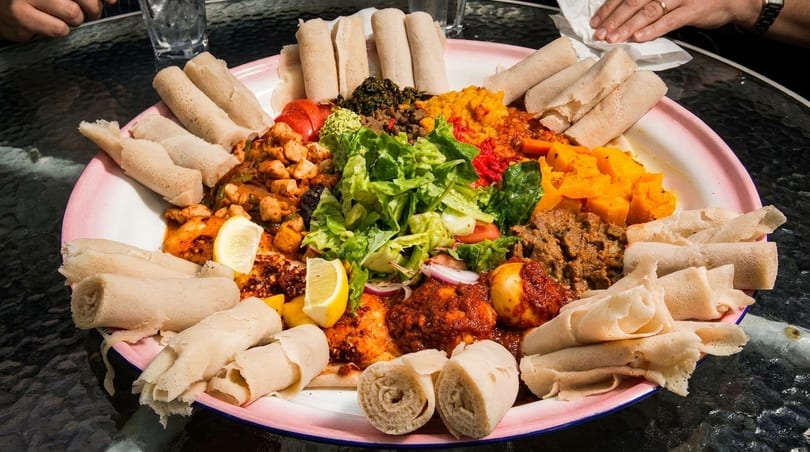 Large platter of colorful Ethiopian food, including injera, stews, and vegetables, on a table.